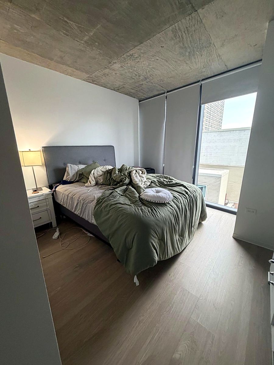 Unmade bed with tangled comforter and cords on the floor
